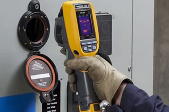 A technician uses a Fluke IR camera to view components inside a porthole window