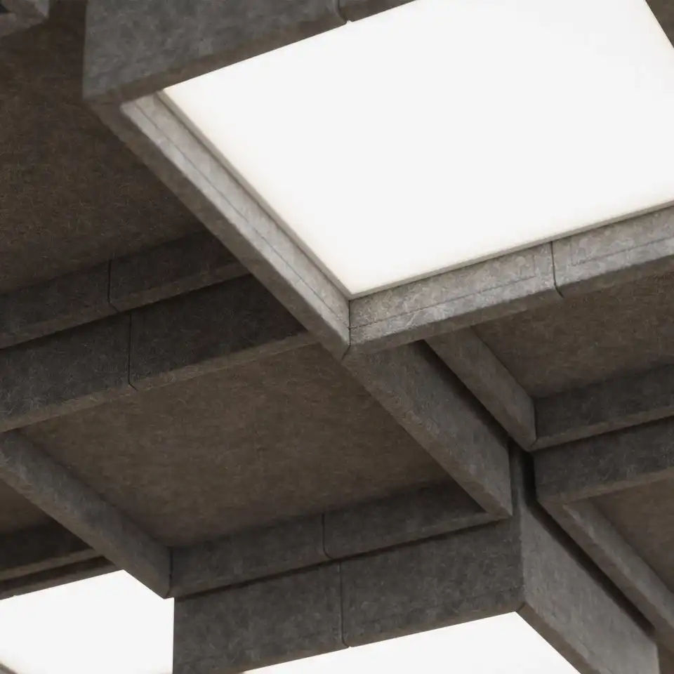 Rectangular light fixtures embedded in an office ceiling amidst dark grey felt acoustic baffles. Each rectangle is slightly offset in height, to give an additional acoustic dampening effect as well as visual interest.