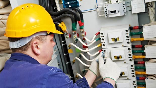 An electrician adjusts wiring at an industrial circuit panel